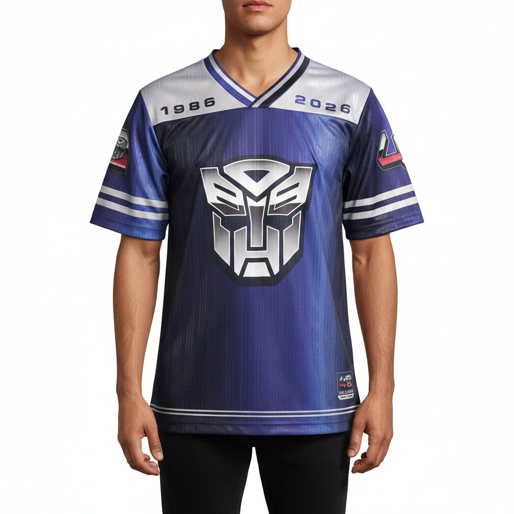 A short-sleeve sports jersey featuring a Transformers logo on the front, hanging on a hanger against a gray concrete floor. The jersey has a blue and purple gradient body, white shoulders, and '1986' and '2028' printed on the chest.